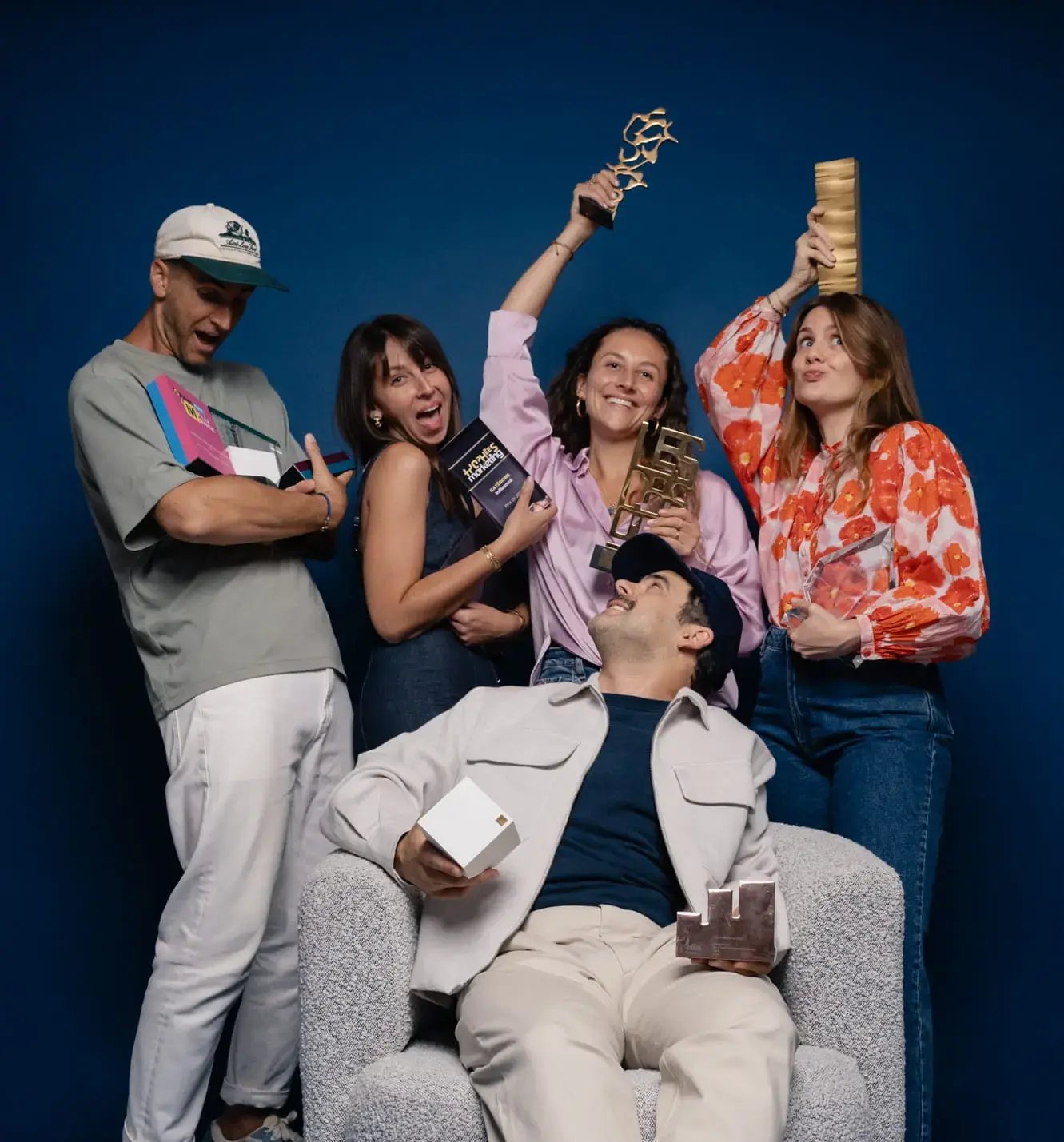 Groupe de 5 personnes avec des trophées dans les mains, dans un studio photo